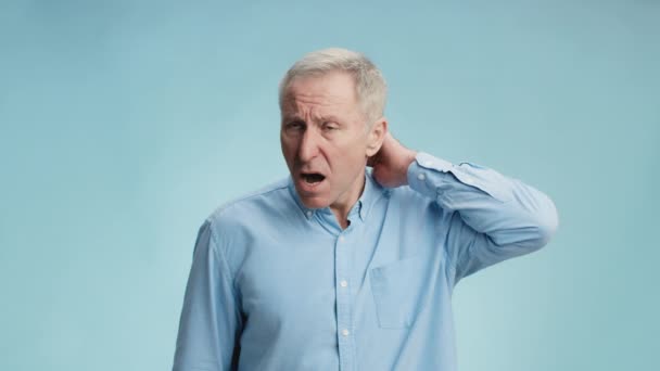 Problemas de saúde do envelhecimento. Homem idoso perturbado que sofre de dor no pescoço, aquecimento e massagem parte do corpo, fundo azul — Vídeo de Stock