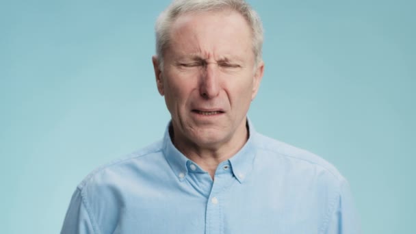 Sensazione di disgusto. Emozionale uomo anziano dai capelli grigi sensazione di odore sgradevole, viso accigliato e bavaglio, sfondo blu — Video Stock