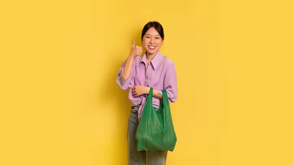 Positivo donna asiatica tenendo riutilizzabile eco bag e mostrando pollice verso l'alto gesto, raccomandando zero rifiuti shopping — Foto Stock