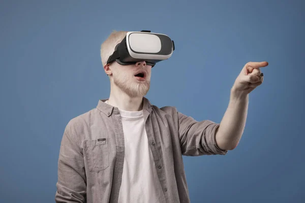 Mondo virtuale in simulazione 3D. Eccitato ragazzo albino in vr occhiali giocando e cercando di toccare qualcosa, sfondo blu — Foto Stock