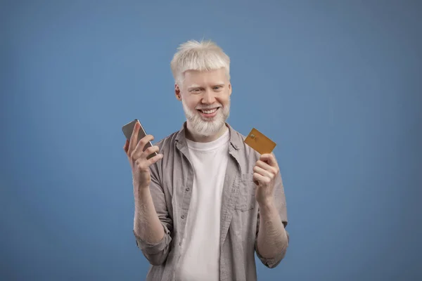 Kredi kartı tutan, cep telefonunu online alışveriş, bankacılık ya da elektronik ödeme için kullanan, nadir bulunan mutlu albino adam. — Stok fotoğraf