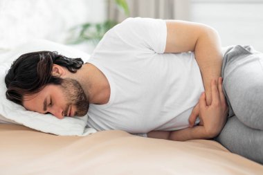 Yatakta yatan ve mide ağrısı çeken bir adam.