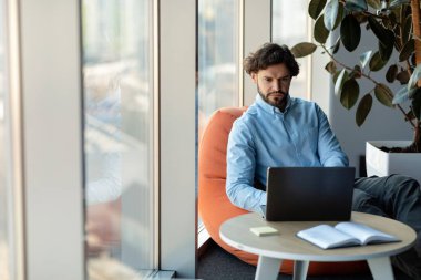 İşadamı koltukta dizüstü bilgisayar kullanıyor.