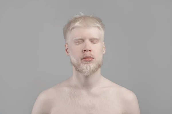 Portrait of young albino man with pale skin, white hair and beard posing with closed eyes against grey background — Stok Foto