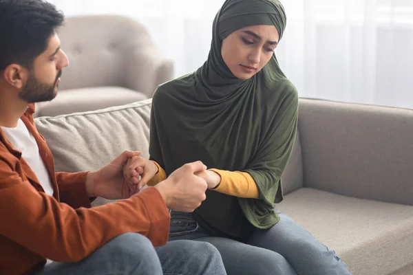 Unhappy Middle Eastern Couple Holding Hands Sitting On Sofa Indoors — Stock Photo, Image