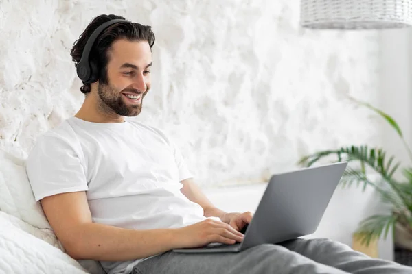 Happy young man sitting on bed, using computer — Foto de Stock