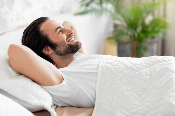 Πλευρική άποψη του χαμογελαστού νεαρός άνδρας χαλαρώνοντας στο κρεβάτι — Φωτογραφία Αρχείου