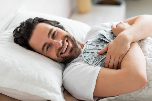 快乐的男人躺在床上，抱着现金 — 图库照片