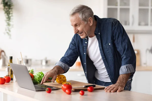 Reifer Mann in Küche liest Rezept im Internet — Stockfoto