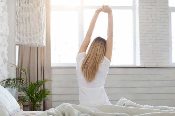 Jól kipihent szőke nő élvezi a boldog reggelt, nyújtózkodik az ágyban — Stock Fotó