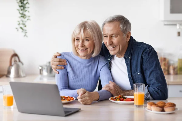 Mutlu yaşlı çift kahvaltı yaparken bilgisayar kullanıyor. — Stok fotoğraf