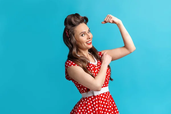 Sexig ung pinup kvinna i retro klänning visar sina biceps muskler på blå studio bakgrund — Stockfoto