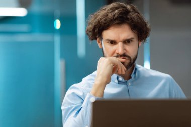 Ofiste otururken dizüstü bilgisayar kullanan odaklanmış bir adam.