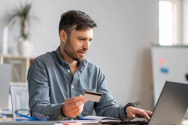 E-ticaret konsepti. Olgun iş adamı kredi kartı ve dizüstü bilgisayar kullanıyor, online alışveriş yapıyor, ofisinde oturuyor.
