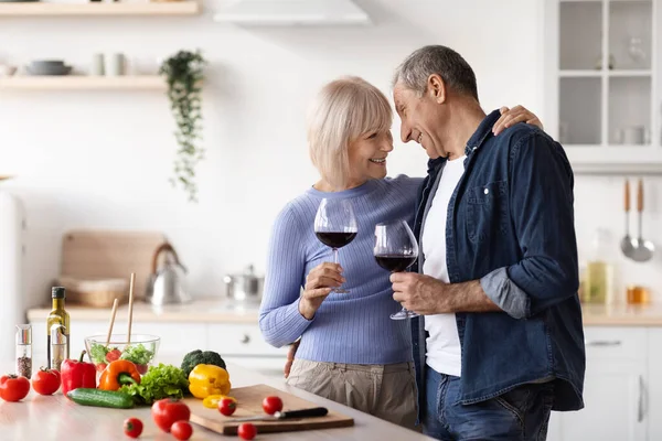 Alegre pareja mayor tintineo con copas de vino en la cocina — Foto de Stock