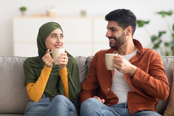 Happy Middle Eastern Couple Having Coffee Holding Cups At Home