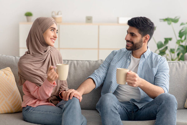 Happy Young Muslim Couple Having Coffee Sitting On Couch Indoor