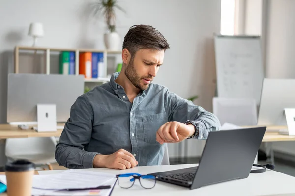 Zakelijke carrière en tijdmanagement. Volwassen zakenman met behulp van laptop en het controleren van de tijd, op zoek naar horloge — Stockfoto