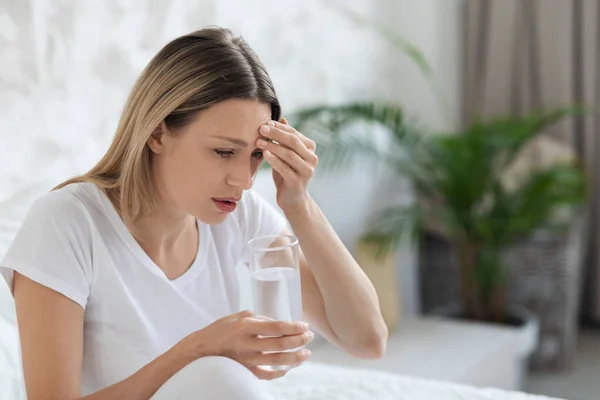 Kranke blonde Dame fühlt sich schlecht, berührt Kopf, Schlafzimmereinrichtung — Stockfoto