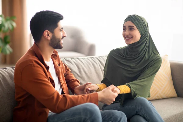 Boldog közel-keleti pár fogja egymás kezét otthon ülve — Stock Fotó