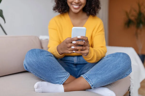 Akıllı telefon kullanan, internette görüntülü sohbet yapan, evdeki kanepede oturan Afro-Amerikan genç bir kadın görüntüsü. — Stok fotoğraf