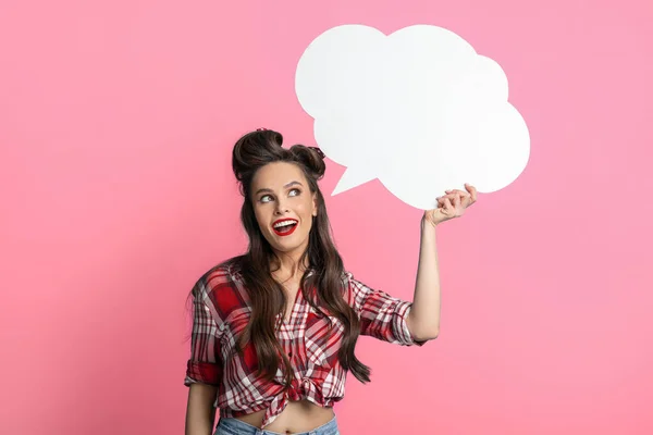 Ung pinup kvinna i retro outfit håller tomt vitt tal bubbla på rosa studio bakgrund — Stockfoto