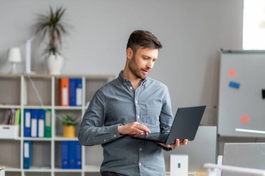 Laptop bilgisayarı kullanan, modern ofiste çalışan, klavyede yazan yakışıklı bir iş adamı.