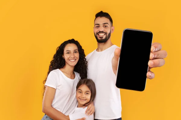 Família do Oriente Médio mostrando tela em branco do celular sobre fundo amarelo — Fotografia de Stock