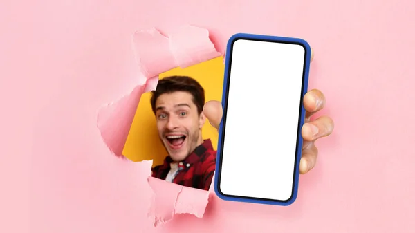 Волнующий парень показывает белый пустой экран смартфона через рваную бумагу — стоковое фото