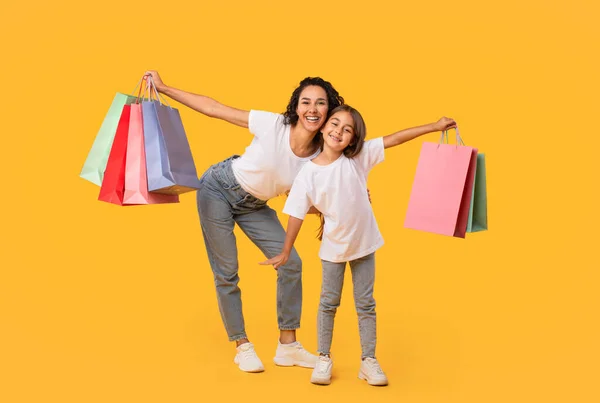 Árabe mamá e hija posando sosteniendo bolsas de compras, fondo amarillo —  Fotos de Stock
