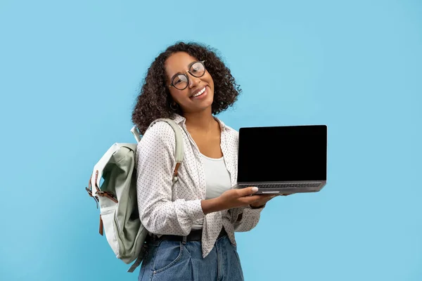 Millennial black female student holding laptop with empty screen for educational website mockup over blue background — Photo