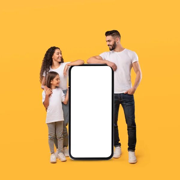 Middle Eastern Family Leaning On Huge Smartphone Screen, Yellow Background — Stockfoto