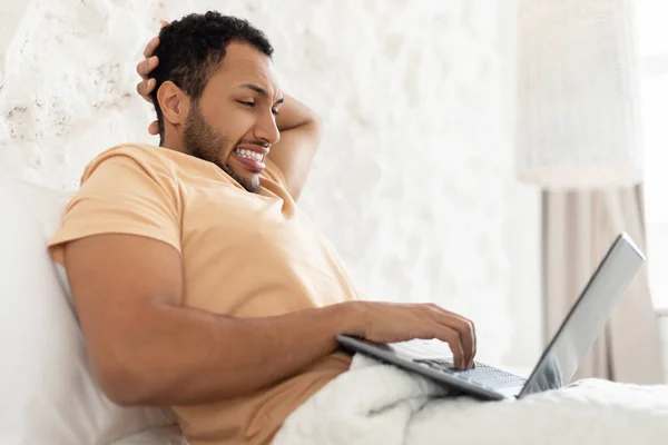 Confused Middle Eastern Man Using Laptop Having Problem In Bedroom