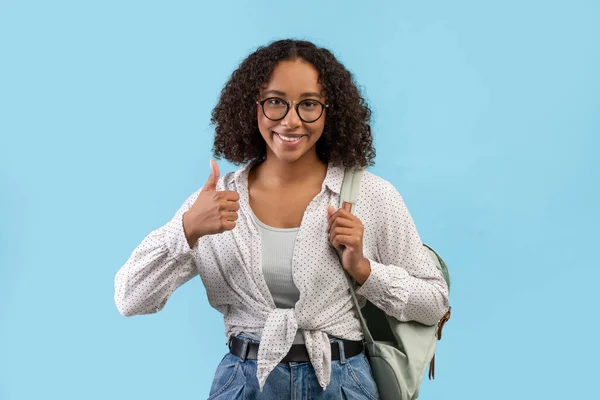 Cheerful African American female student with backpack showing thumb up gesture over blue studio background — Foto Stock