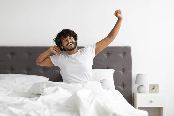 Well-rested indian guy in pajamas stretching in bed — Stock fotografie