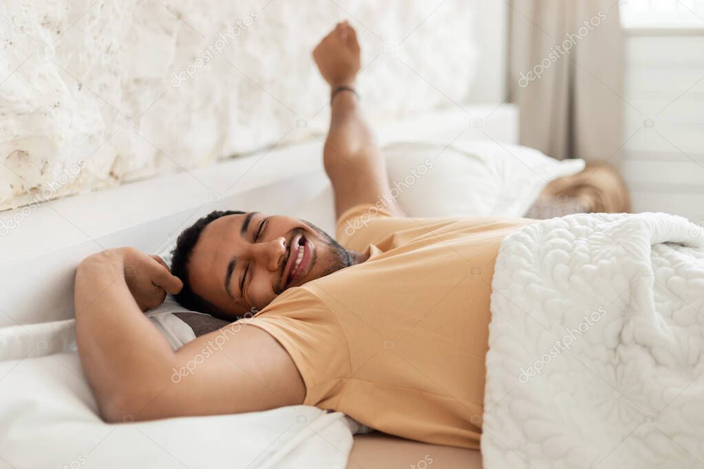 Happy Arabic Male Awakening Yawning Stretching Arms Lying In Bedroom