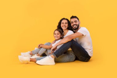 Arabic Father, Mother And Daughter Hugging Sitting Over Yellow Background
