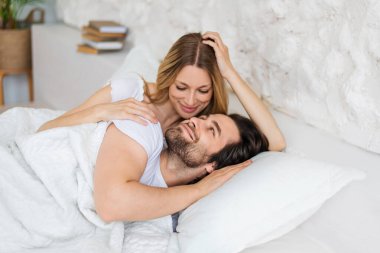 Affectionate young woman hugging her boyfriend after waking up in morning, lying on bed at home
