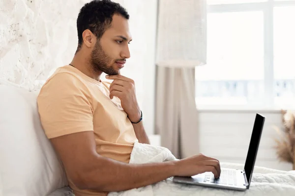 Arabic Male Freelancer εργασίας σε απευθείας σύνδεση σε φορητό υπολογιστή κάθεται στην κρεβατοκάμαρα — Φωτογραφία Αρχείου