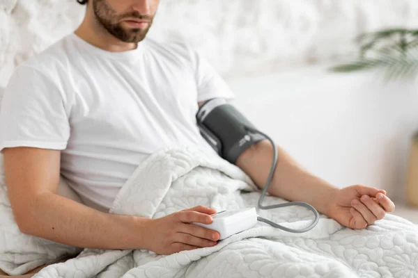 Обрізаний чоловік перевіряє кров'яний тиск вдома, інтер'єр спальні — стокове фото