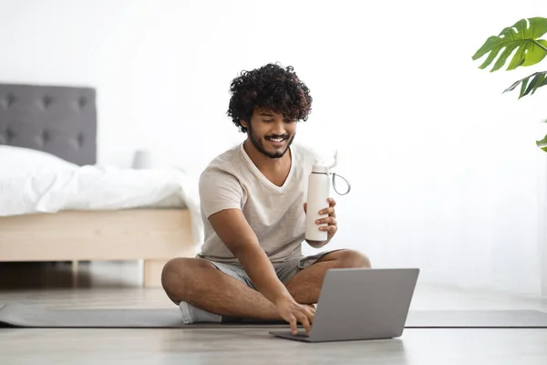 Happy guy sitting on yoga mat with bottle of water — Foto Stock