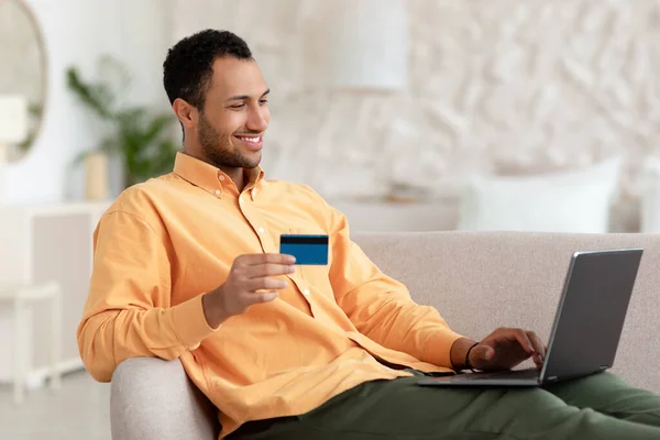 Koltukta oturan gülümseyen adam bilgisayar ve kredi kartı kullanıyor. — Stok fotoğraf