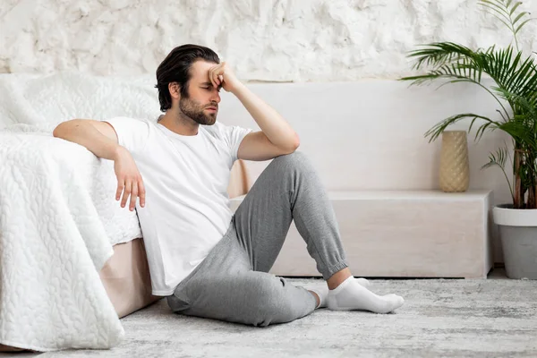 Grumpy millennial man feeling down, bedroom interior