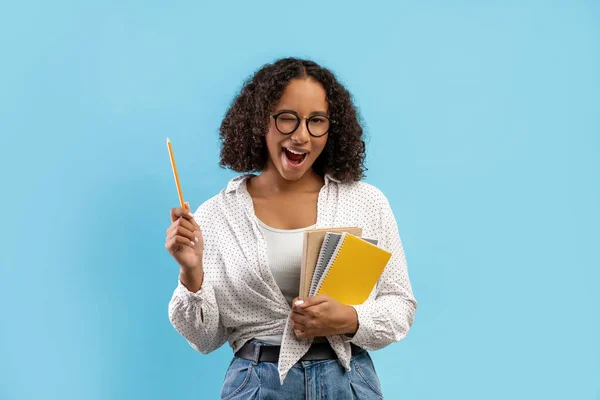 Portrait of cheerful young female student with notebooks having great idea, pointing pencil up and winking — Stock Photo, Image