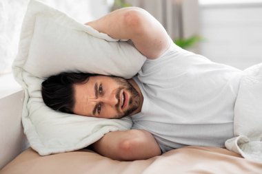 Young man in bed covering head with pillow