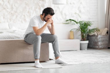 Lonely young man sitting on bed alone, copy space
