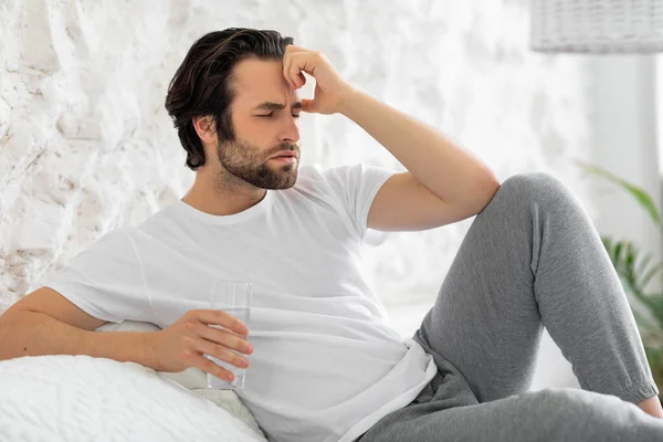 Man taking glass of water in bed, suffering from hangover — Stockfoto