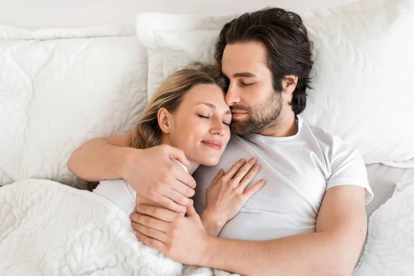 Top view of young affectionate couple sleeping in bed, embracing each other. Loving relationships and marriages — стоковое фото