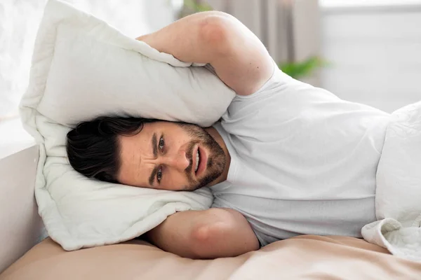 Mladý muž v posteli pokrývající hlavu s polštářem — Stock fotografie