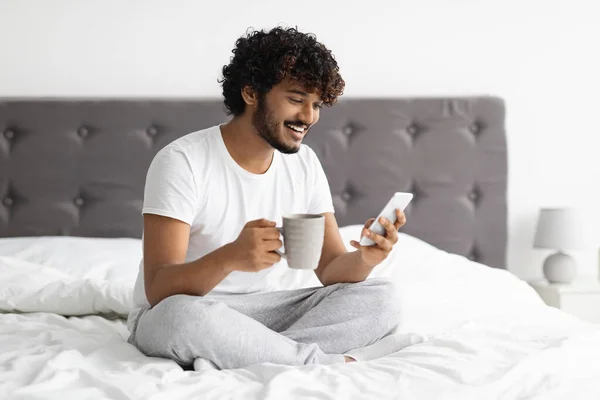 Χαρούμενος σκουρόχρωμος άνδρας πίνει καφέ και χρησιμοποιεί smartphone — Φωτογραφία Αρχείου
